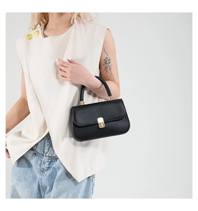 Close-up of black leather saddle bag with gold metal clasp and single top handle detail