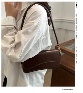 Detail of dark brown leather baguette bag with wavy flap design and gold hardware