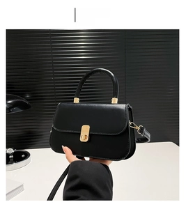 Detail of black leather crossbody bag featuring an elegant gold lock and curved top handle