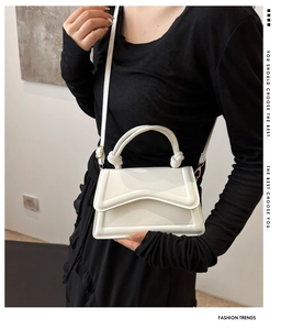 Detail of white textured handbag with wavy flap and woven handle worn by model