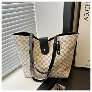 Detail of monogram print tote bag featuring black M patterns and metal stud closure