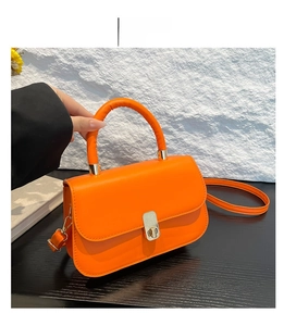 Detailed view of an orange leather bag with retro metal clasp and textured stitching