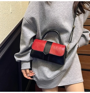 Détail du sac bandoulière contrasté bordeaux et noir avec texture cuir et boucles dorées
