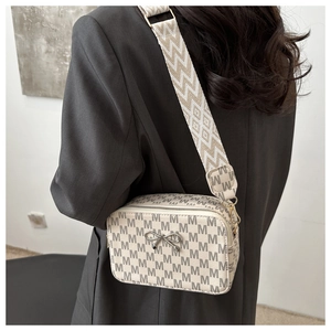 Detail of cream square crossbody bag with M pattern and silver metal bow on strap