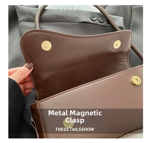 Detail view of the secure gold magnetic buckle closure on a brown leather shoulder bag