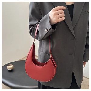 Close-up of minimalist red crescent shoulder bag made of smooth leather with matching strap