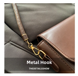 Close-up of polished gold-tone hardware hook on a dark brown leather shoulder bag
