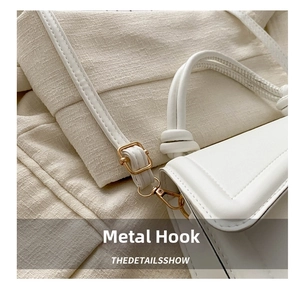 Detailed macro view of high-quality gold metal hooks on a white minimalist shoulder bag