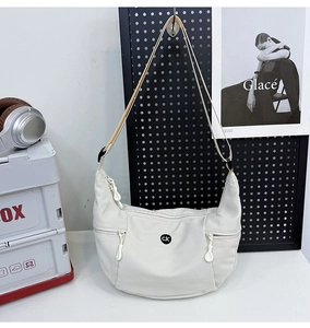 Détail d'un sac demi-lune en nylon blanc crème montrant la bandoulière réglable et les cordons