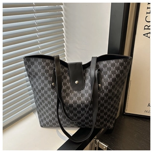 Close-up of geometric M-pattern tote bag with black leather straps on white ledge