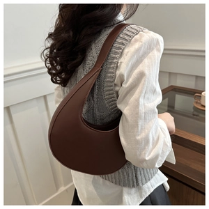 Lifestyle view of brown crescent shoulder bag worn underarm with minimalist matte finish