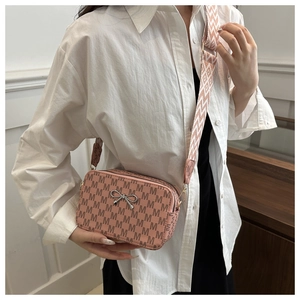 Detailed shot of pink camera bag with letter pattern, metal bow, and wide strap
