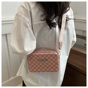 Detail of pink crossbody camera bag with M-pattern print and woven wide shoulder strap