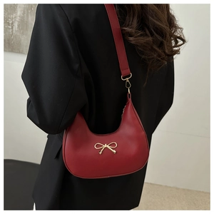 Nahaufnahme einer roten Hobo-Tasche aus Leder mit goldener Schleife auf schwarzem Sakko