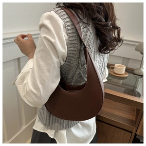 Close-up of a brown crescent-shaped shoulder bag worn by a model in a warm room