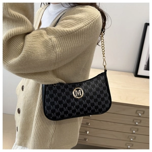 Detail of black underarm bag with grey M pattern and gold chain strap on model