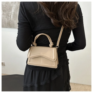 Detail van beige leren tas met gegolfde flap en geknoopte handgreep bij een model
