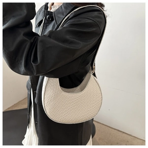 Detailed view of a white crescent shoulder bag with woven texture on a model's arm