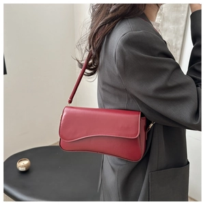Close-up of a burgundy underarm bag with curved flap on a grey suit model