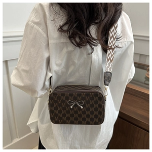Detail of a brown camera bag with M-pattern print and a wide chevron shoulder strap