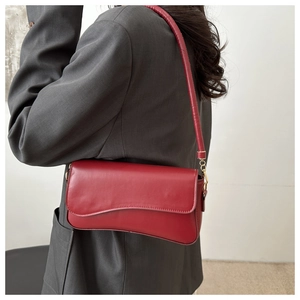 Detail of dark red leather baguette bag with magnetic flap worn by a model