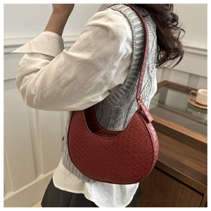 Detail of dark red crescent shoulder bag featuring premium woven texture on a model