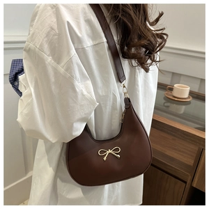 Detail der dunkelbraunen halbmondförmigen Tasche mit goldener Schleife und Schultergurt
