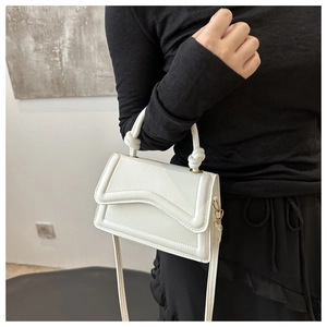 Detailopname van witte vierkante handtas met gegolfde klep en knoophandvat