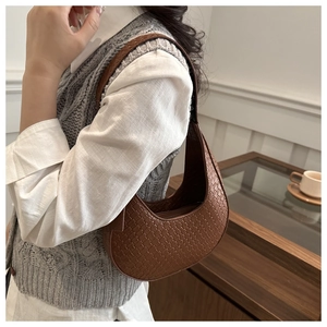 Close-up of woven dark brown leather crescent bag on shoulder with fine grid texture