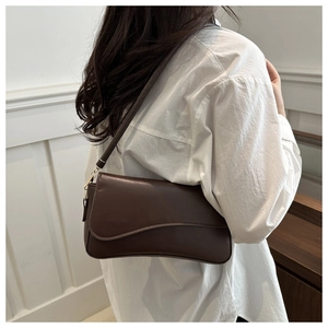 Detail of dark brown leather handbag with wavy flap design on model shoulder