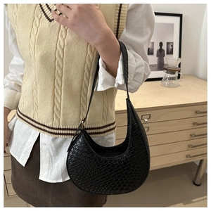 Detail shot of black crescent shoulder bag with crocodile pattern on a leather surface