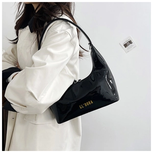 Close-up of black glossy patent leather hobo bag with gold letter logo and slim shoulder strap