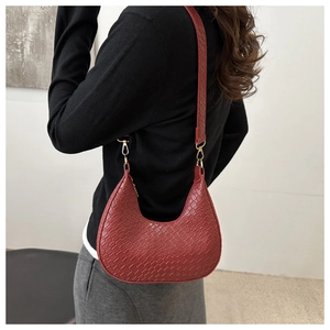 Detail of dark red woven crescent bag worn by model, showing texture and shoulder fit