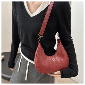 Detail of burgundy woven crescent bag showing leather texture and gold hardware on model