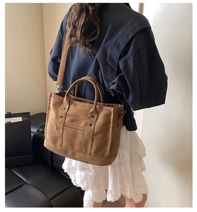 Brown canvas tote bag with wide shoulder strap shown on model from back view