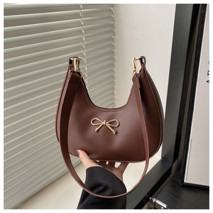 Detail einer braunen Halbmondtasche mit goldener Metallschleife und glatter Lederstruktur