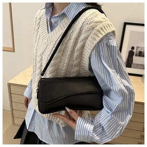 Detail of minimalist black leather shoulder bag with elegant asymmetrical flap and gold hardware