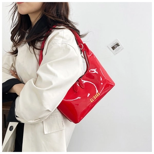 Detail of red patent leather baguette bag with gold logo shown on model shoulder