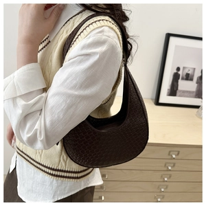 Detail of dark brown woven crescent saddle bag worn by model in a minimalist setting