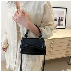 Detail view of a black mini square bag with wave stitching and top handle on a model