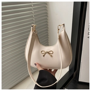 Nahaufnahme einer cremefarbenen Hobo-Tasche mit dekorativer goldener Metallschleife