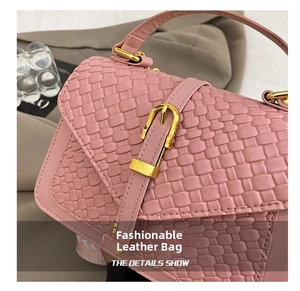 Close-up of pink woven handbag featuring decorative belt and gold metallic buckle hardware