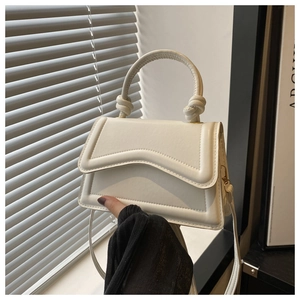 Detail van de golvende flap en geknoopte handgreep van de crèmewitte crossbodytas
