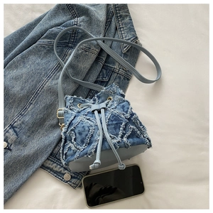 Dettaglio borsa a secchiello in denim blu con chiusura a coulisse e bordi sfilacciati