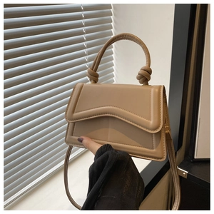 Detail van beige vierkante handtas met golvende flap en decoratieve geknoopte greep