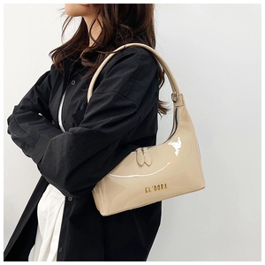 Close-up of beige patent leather shoulder bag with gold letter design and metal zippers