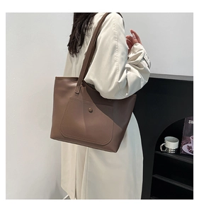 Detail view of large dark brown leather tote bag with functional snap button front pocket