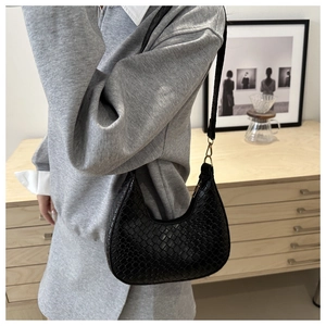 Close-up of a black woven crescent underarm bag worn by a model in a modern interior