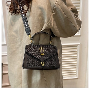 Close-up of black woven texture leather handbag with gold buckle and patterned strap