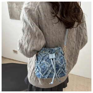 Dettaglio della borsa a secchiello in denim trapuntato con bordi sfilacciati indossata